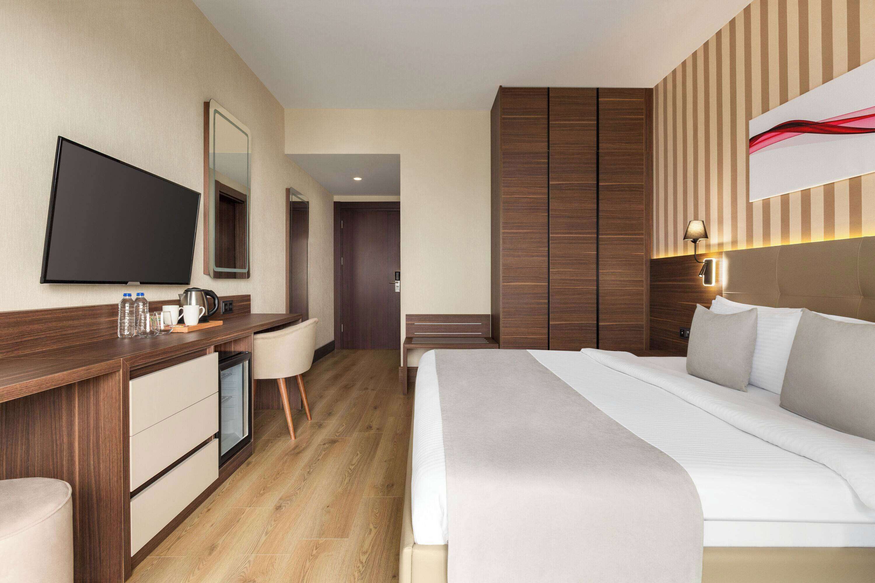 A hotel room with a bed, a desk with a television, a mirror, and a wardrobe.