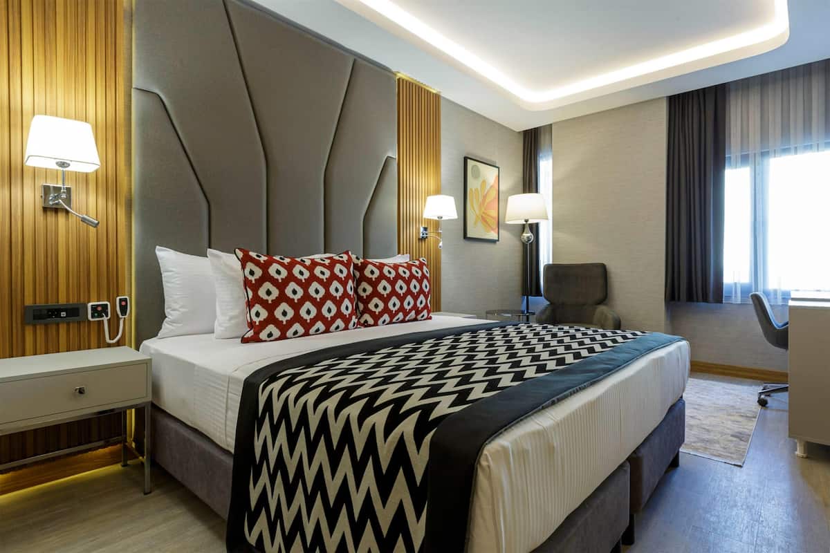 A modern hotel room with a large bed, two bedside lamps, a desk, and a chair.