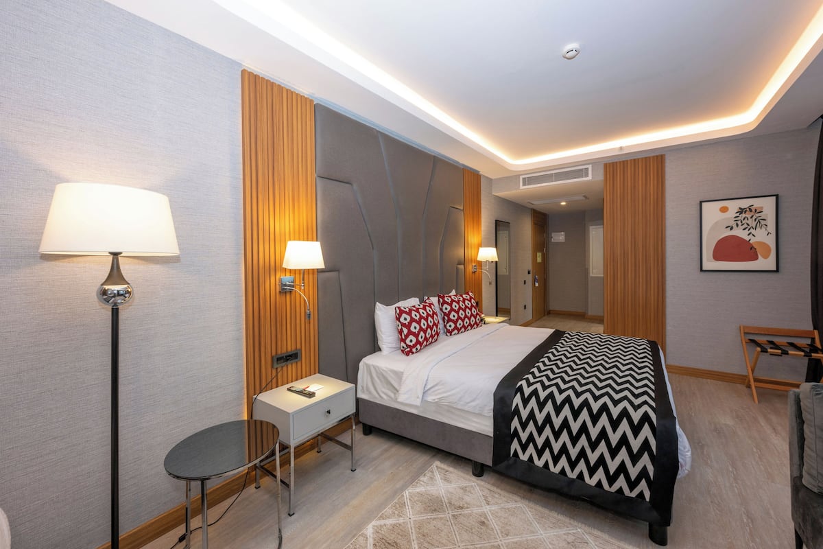 A modern hotel room with a bed, bedside lamps, a desk, and a chair.