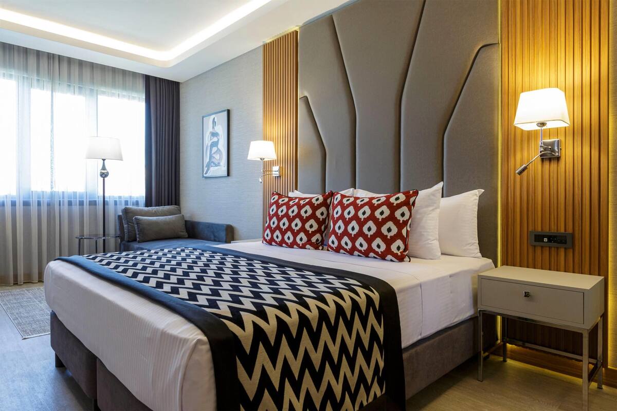 A hotel room with a large bed, two bedside lamps, a nightstand, and a wall-mounted control panel.
