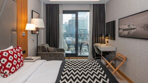 A hotel room with a bed, a desk, a chair, a balcony with a view of the city, and a large window.