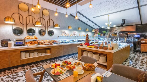 A breakfast buffet with various food items and a seating area with chairs and a table.
