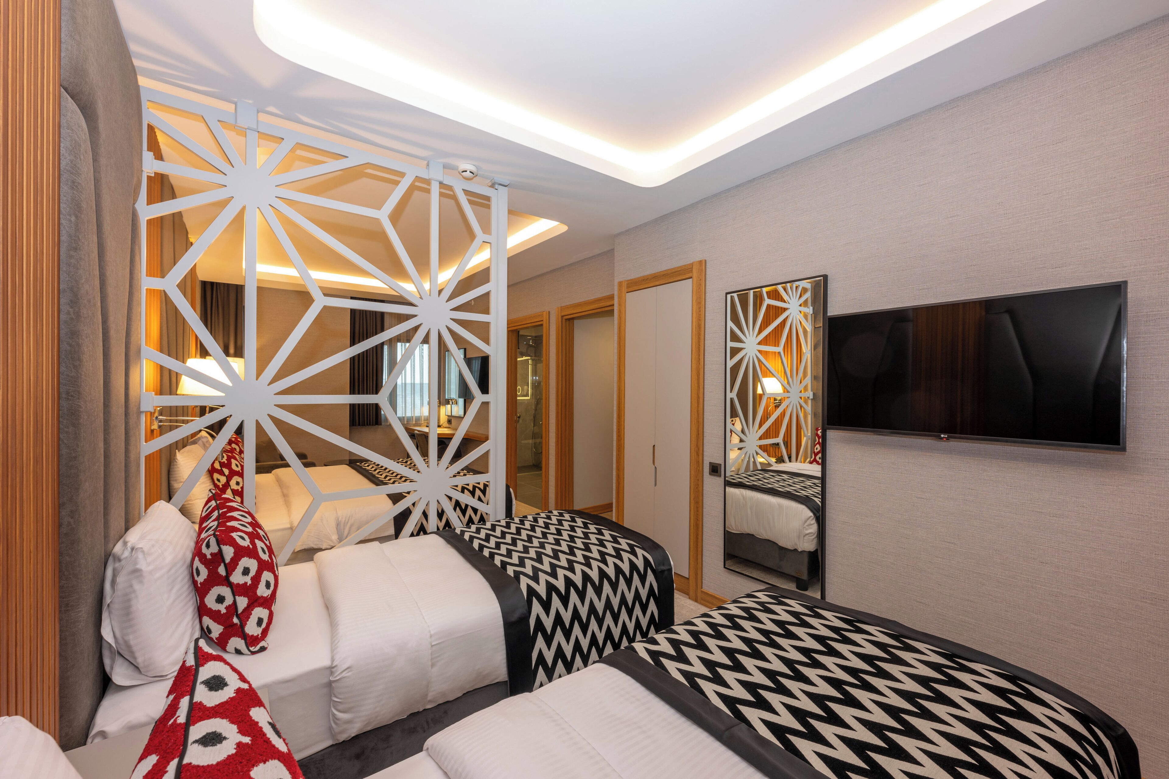 A modern hotel room with a large bed, a TV mounted on the wall, and a decorative white partition.