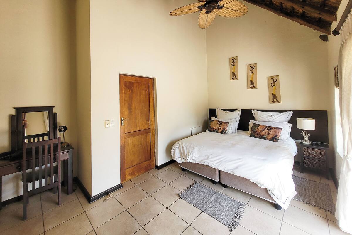 Een slaapkamer met een bed, een houten deur, een plafondventilator en een nachtkastje met een lamp.