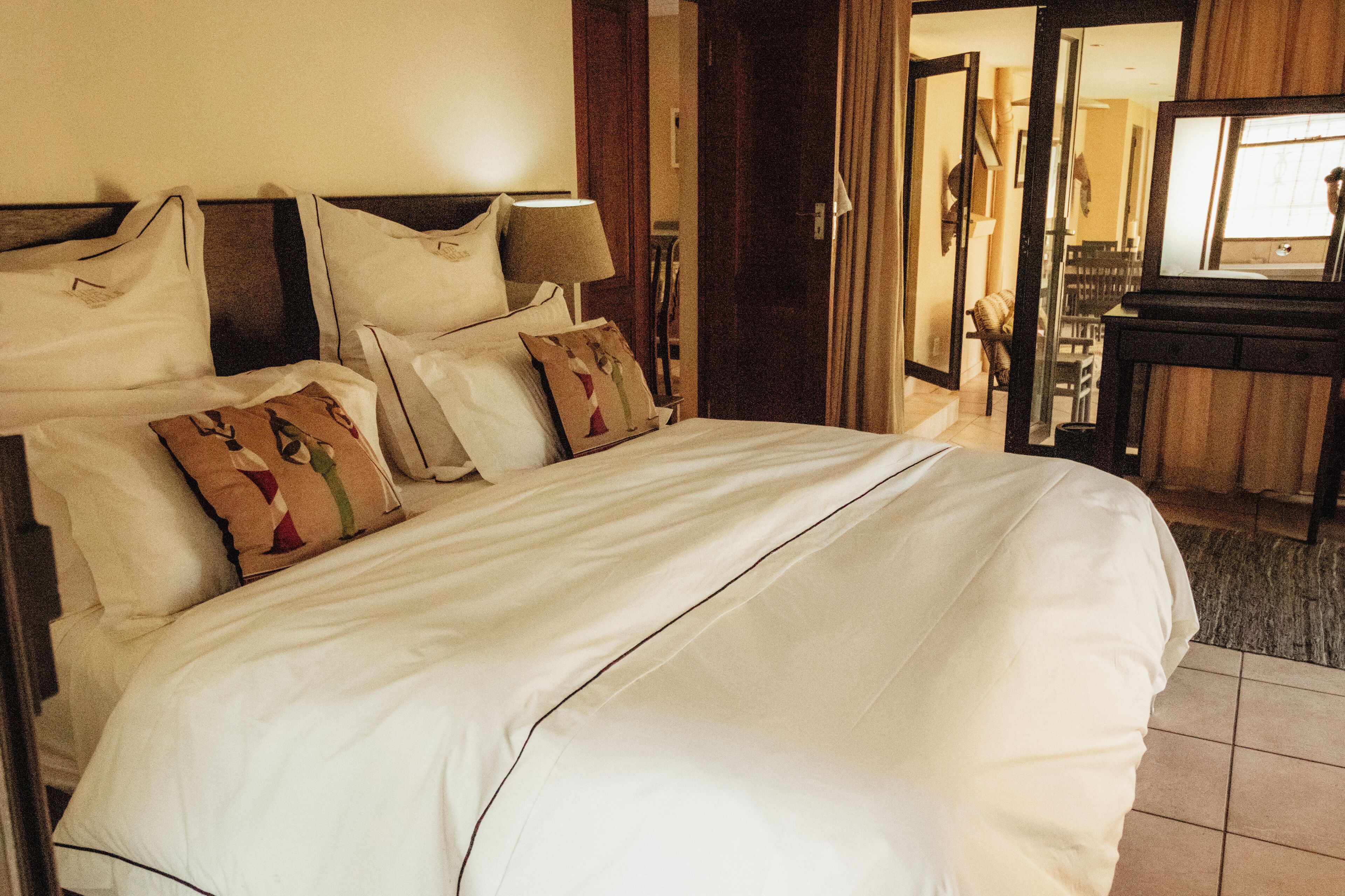 Una habitación de hotel con una cama grande, varios almohadones, una mesita de noche y un espejo.