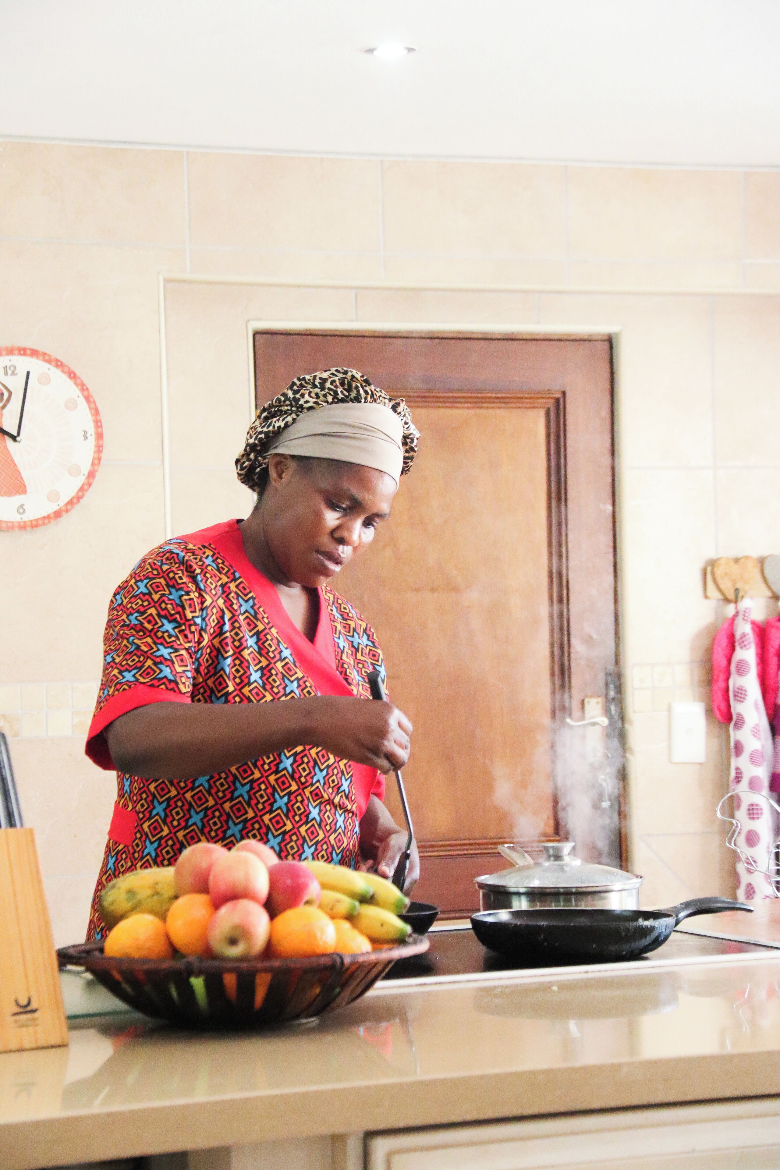 A person cooking in a kitchen with a stove, a pot, and a bowl of fruit.