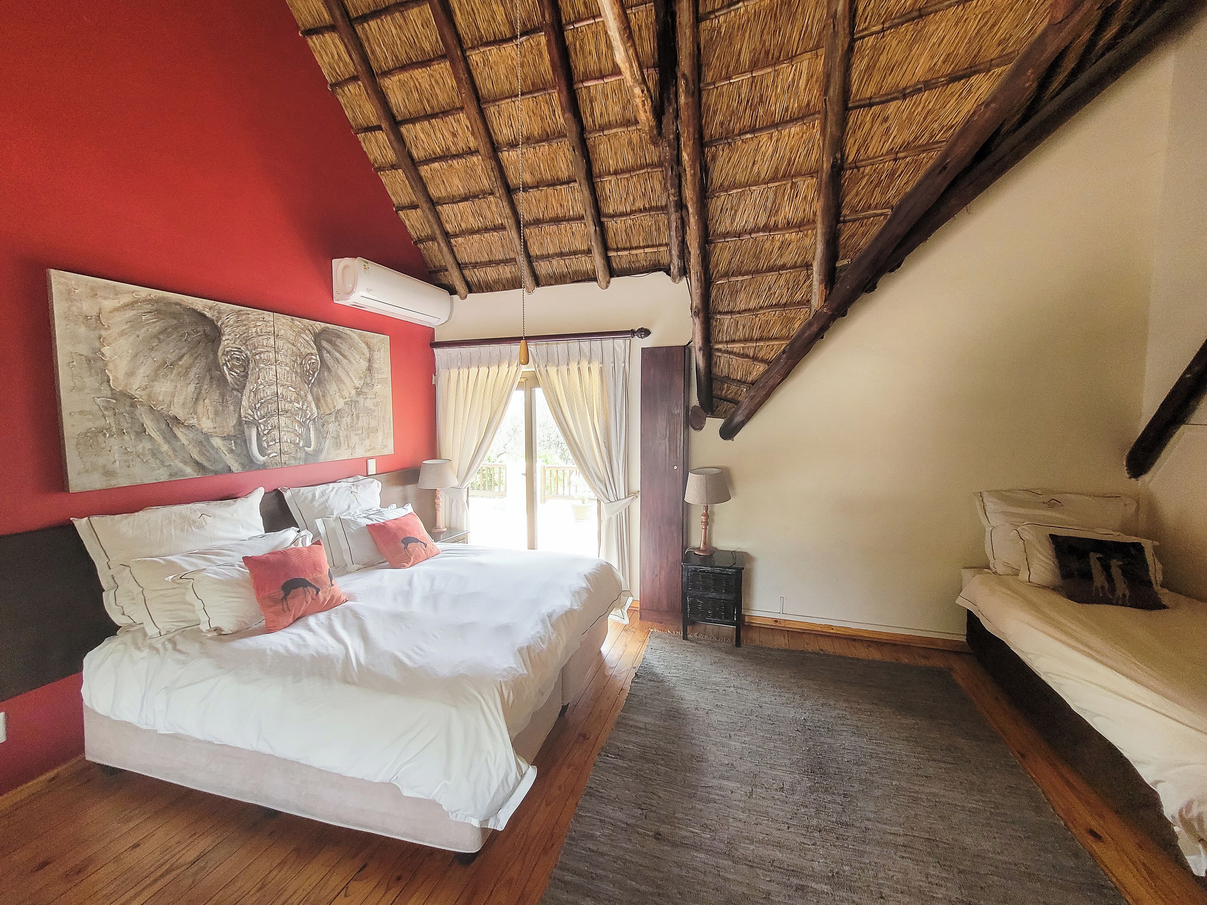 A bedroom with a bed, a nightstand, a lamp, a painting, and a balcony.
