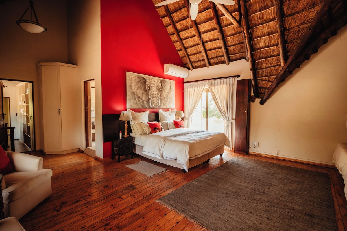 Ruime slaapkamer met een groot bed, een rode accentmuur, houten vloeren en een schuine plafond.