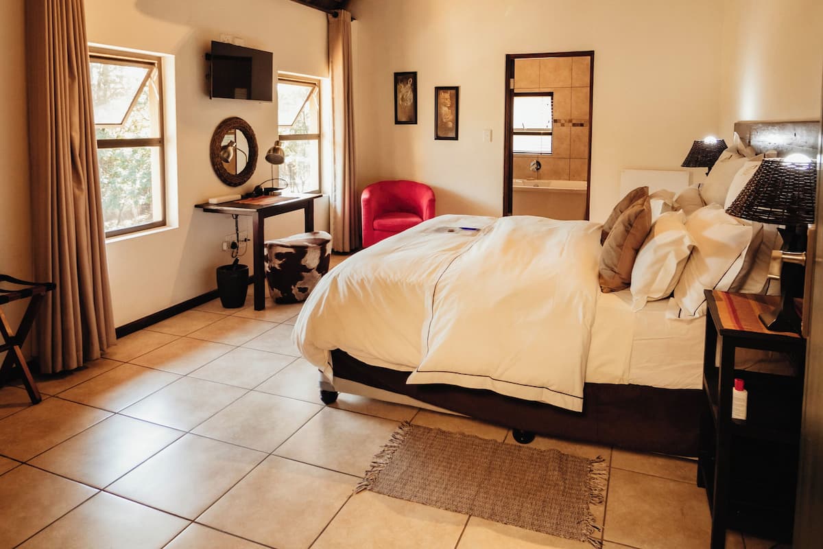 Een slaapkamer met houten plafond, een bed, een bureau, een stoel en een raam.