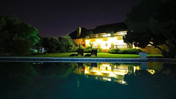 Une vue nocturne d’une maison avec une piscine, où se reflètent les lumières et le bâtiment.