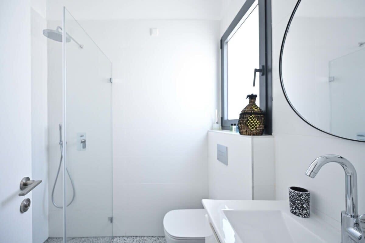 A modern bathroom with a glass shower enclosure, a toilet, a sink with a mirror, and a decorative item on the windowsill.