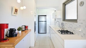 Une cuisine moderne avec des meubles blancs, un réfrigérateur en acier inoxydable, une cuisinière à gaz et une machine à café.