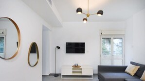 A modern living room with a flat-screen TV, a sofa, a coffee table, and a floor lamp. - Stylish 2BR in Central Tel Aviv by HolyGuest (Tel Aviv-Yafo)