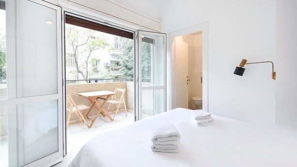 A modern hotel room with a large bed, a balcony with a table and chairs, and a view of the outside. - Stylish 2BR in Central Tel Aviv by HolyGuest (Tel Aviv-Yafo)