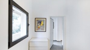 A hallway with a white bench, a framed poster on the wall, and a door leading to another room. - Stylish 2BR in Central Tel Aviv by HolyGuest (Tel Aviv-Yafo)