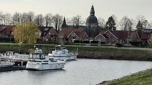 A canal with boats docked, surrounded by residential buildings and a prominent church steeple. - 2 Bedroom Apartment in Haren (Ems) (Haren (Ems))