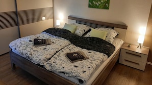 A neatly made bed with floral bedding, a bedside lamp, and a small nightstand with a plant. - 2 Bedroom Apartment in Haren (Ems) (Haren (Ems))