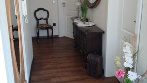A hallway with wooden flooring, a wooden chair, a dresser with a mirror, and a vase with flowers. - 2 Bedroom Apartment in Haren (Ems) (Haren (Ems))