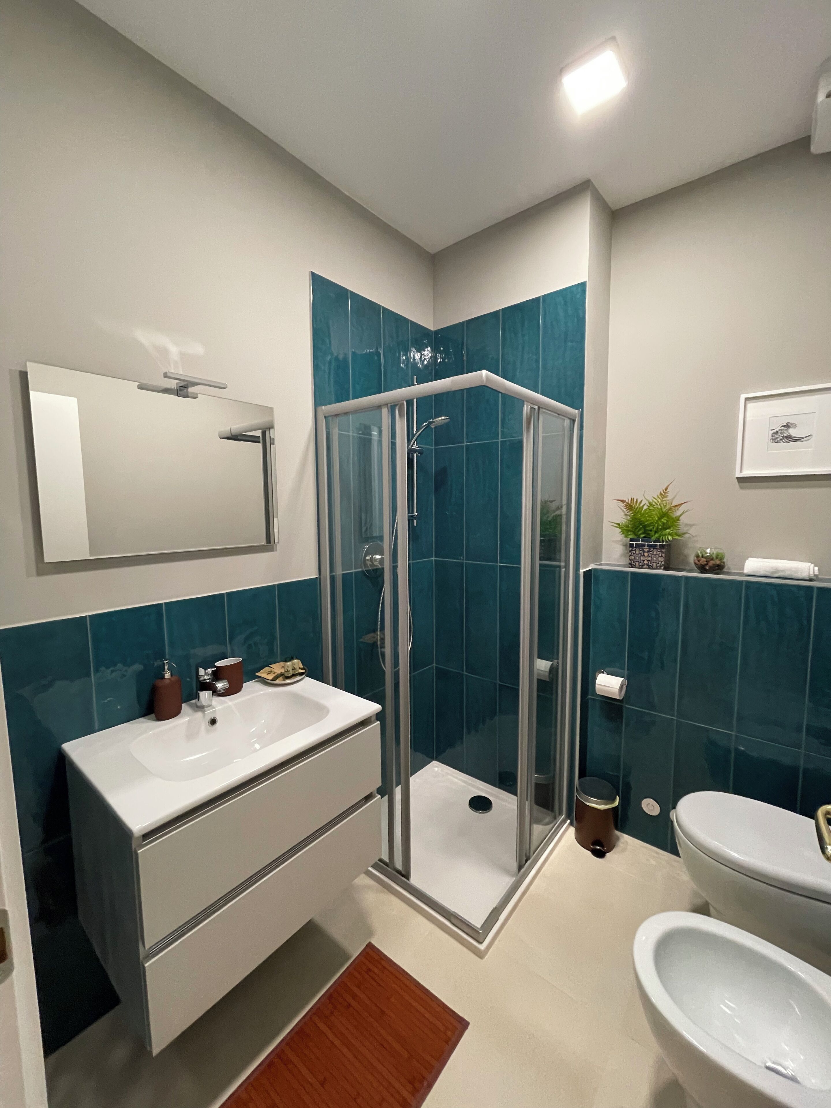 A bathroom with a glass-enclosed shower, a white sink, a toilet, and a mirror.