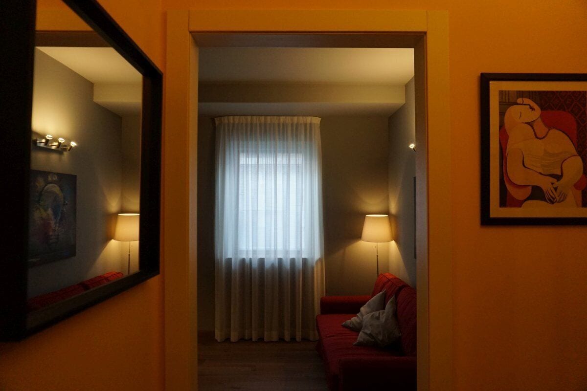 A hotel room with a red sofa, a standing lamp, a large mirror, and a painting on the wall.
