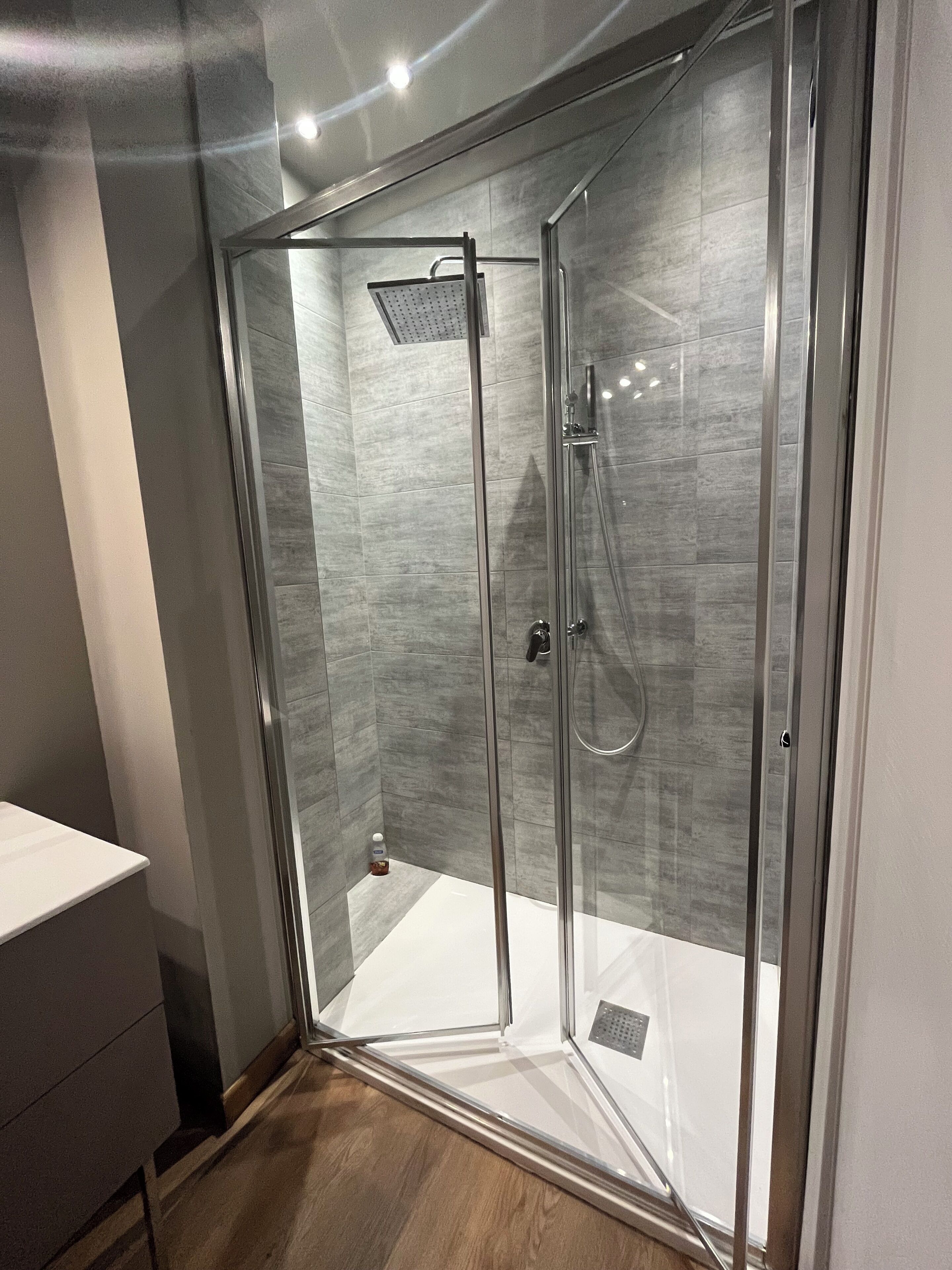 Un baño moderno con mampara de vidrio, ducha de mano y grifo empotrado.