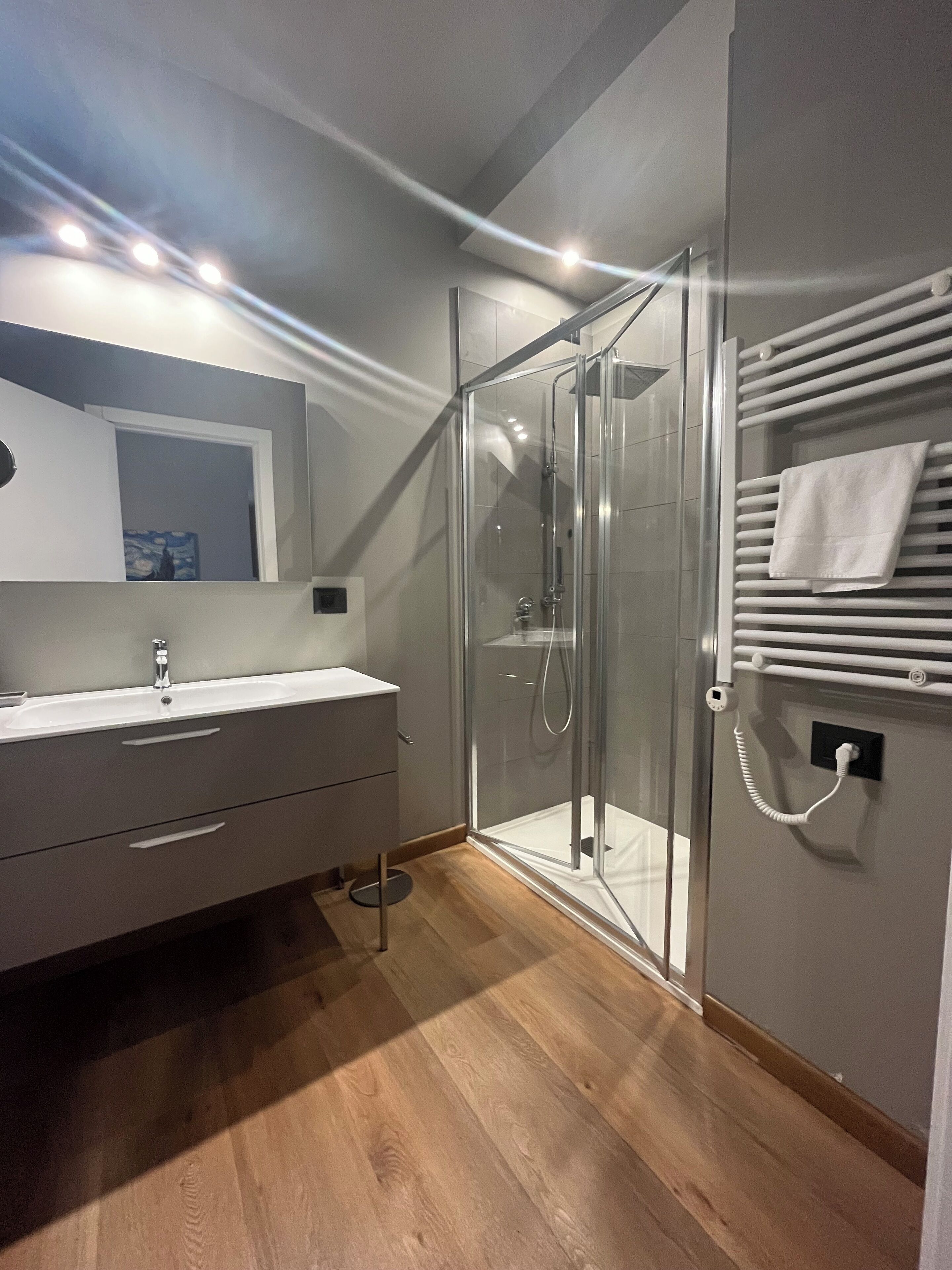 A modern bathroom with a glass shower enclosure, a white vanity with a mirror, and a towel rack with a towel.