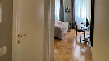 A hotel room with a bed, a desk with a chair, and an air conditioning unit.