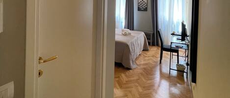 A hotel room with a bed, a desk with a chair, and an air conditioning unit.