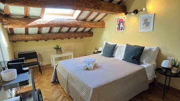 A bedroom with a large bed, wooden beams, a skylight, a desk, and a chair.