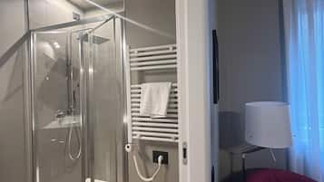 A hotel room with a glass-enclosed shower, a white towel rack, a red chair, and a lamp.