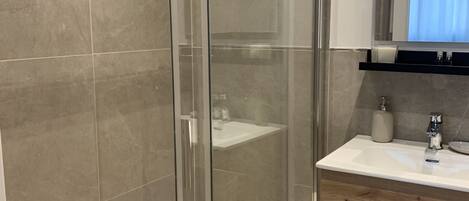 Een moderne badkamer met een douchecabine van glas, een wastafel en een spiegel erboven.