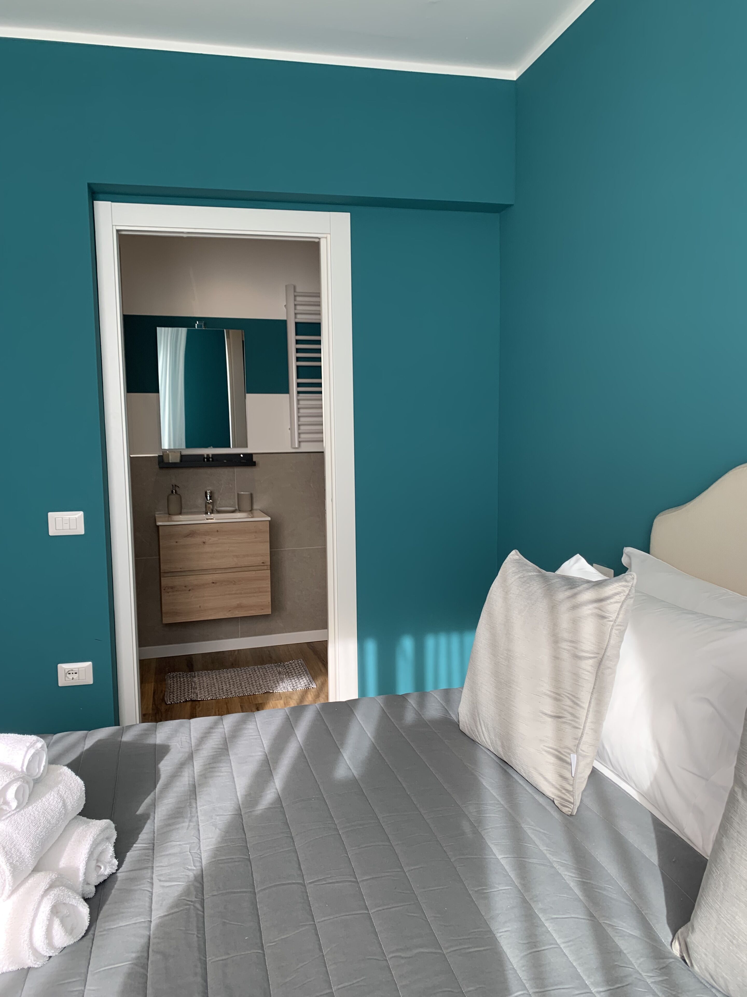 A bedroom with teal walls, a bed with white bedding, a wooden dresser, and a mirror above the mirror.