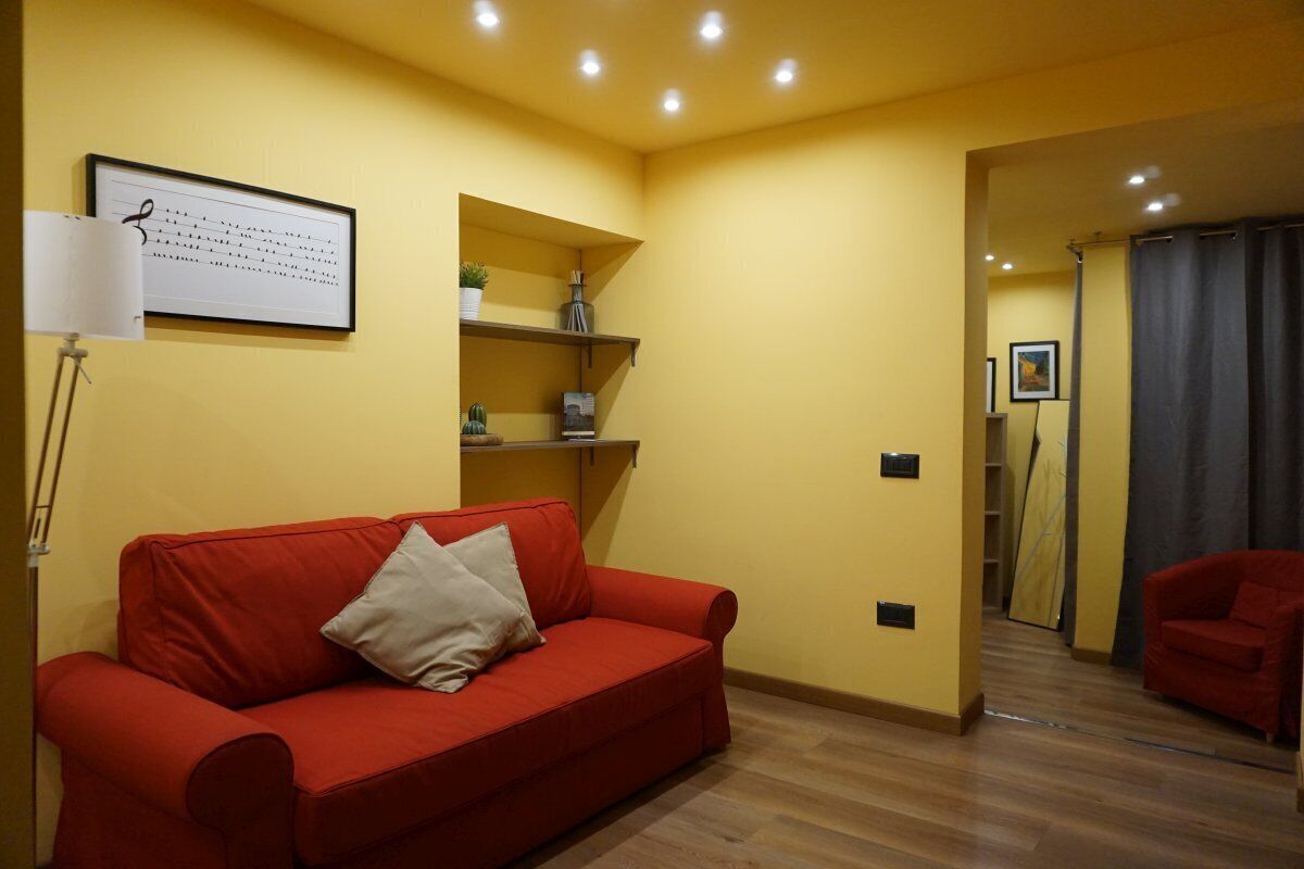 Une pièce avec un canapé rouge, une lampe blanche et une étagère ornée d’objets décoratifs.