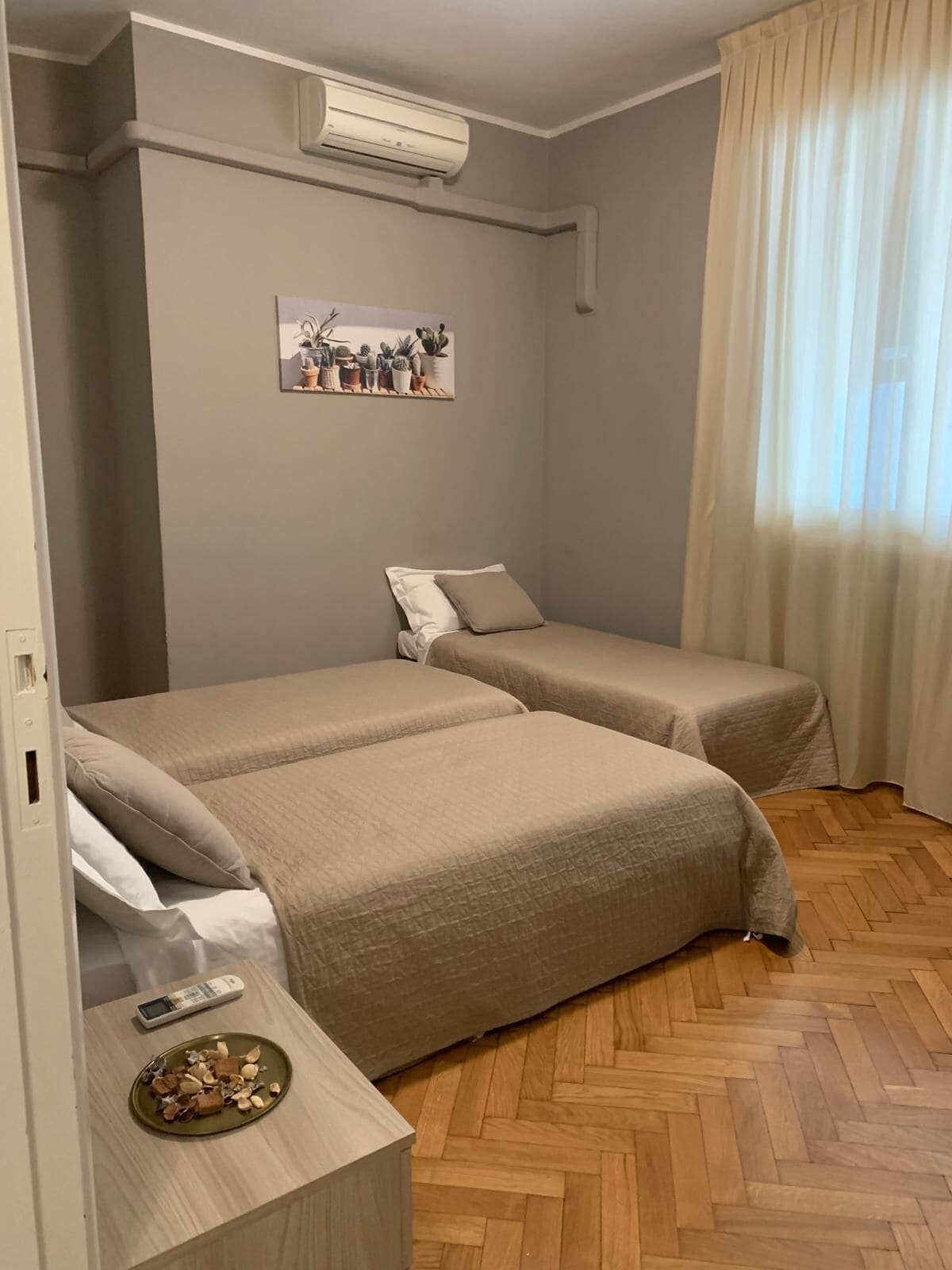 Une chambre avec deux lits, un climatiseur fixé au mur, une petite table avec une assiette de nourriture et une fenêtre avec des rideaux.