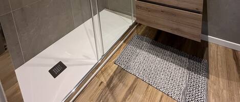 Un baño moderno con cabina de ducha de vidrio, tocador de madera y espejo sobre el lavabo.