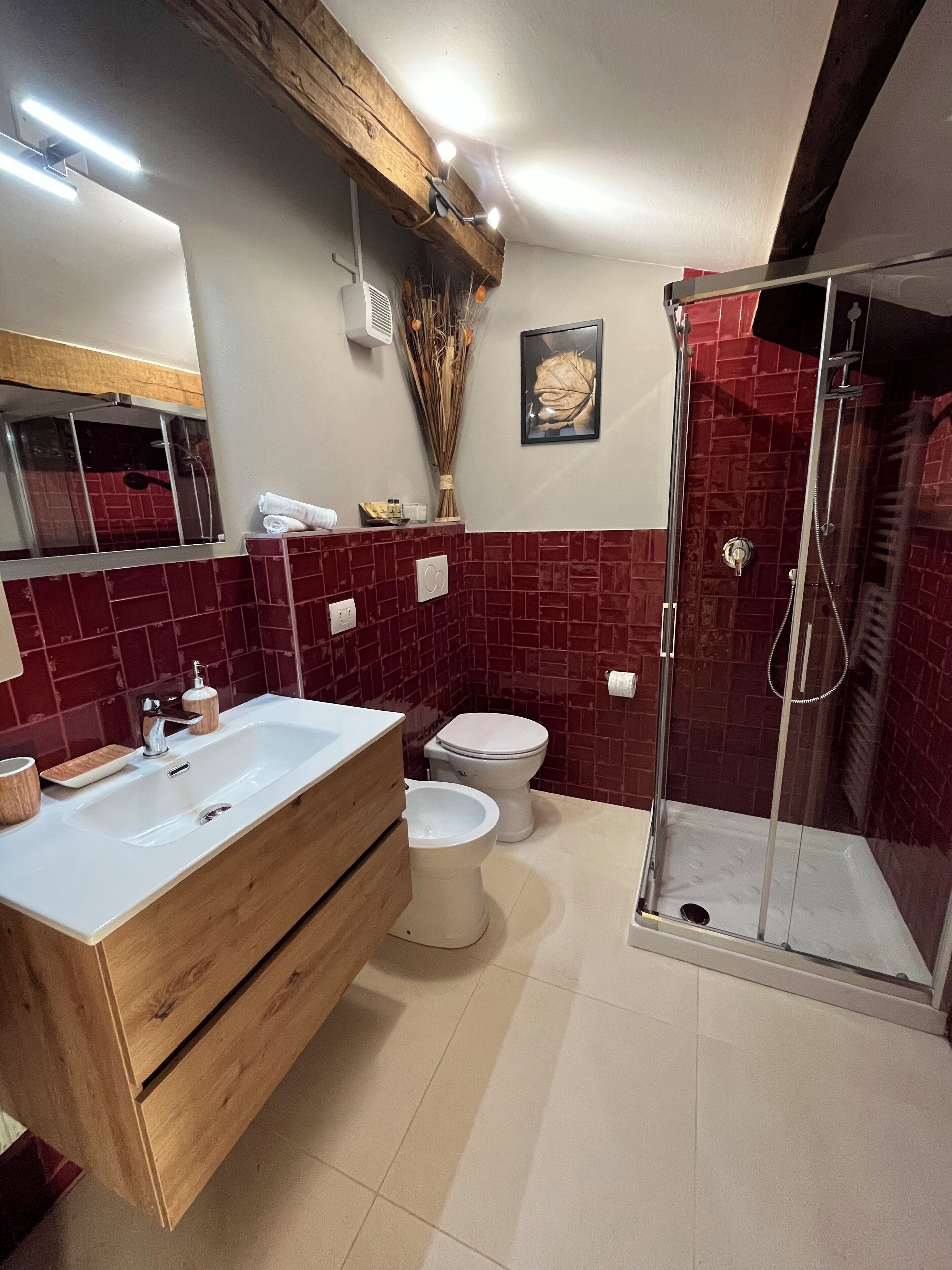 Un baño con tocador de madera, un lavamanos blanco, inodoro y cabina de ducha con mampara de vidrio.