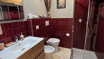 Un baño con tocador de madera, un lavamanos blanco, inodoro y cabina de ducha con mampara de vidrio.
