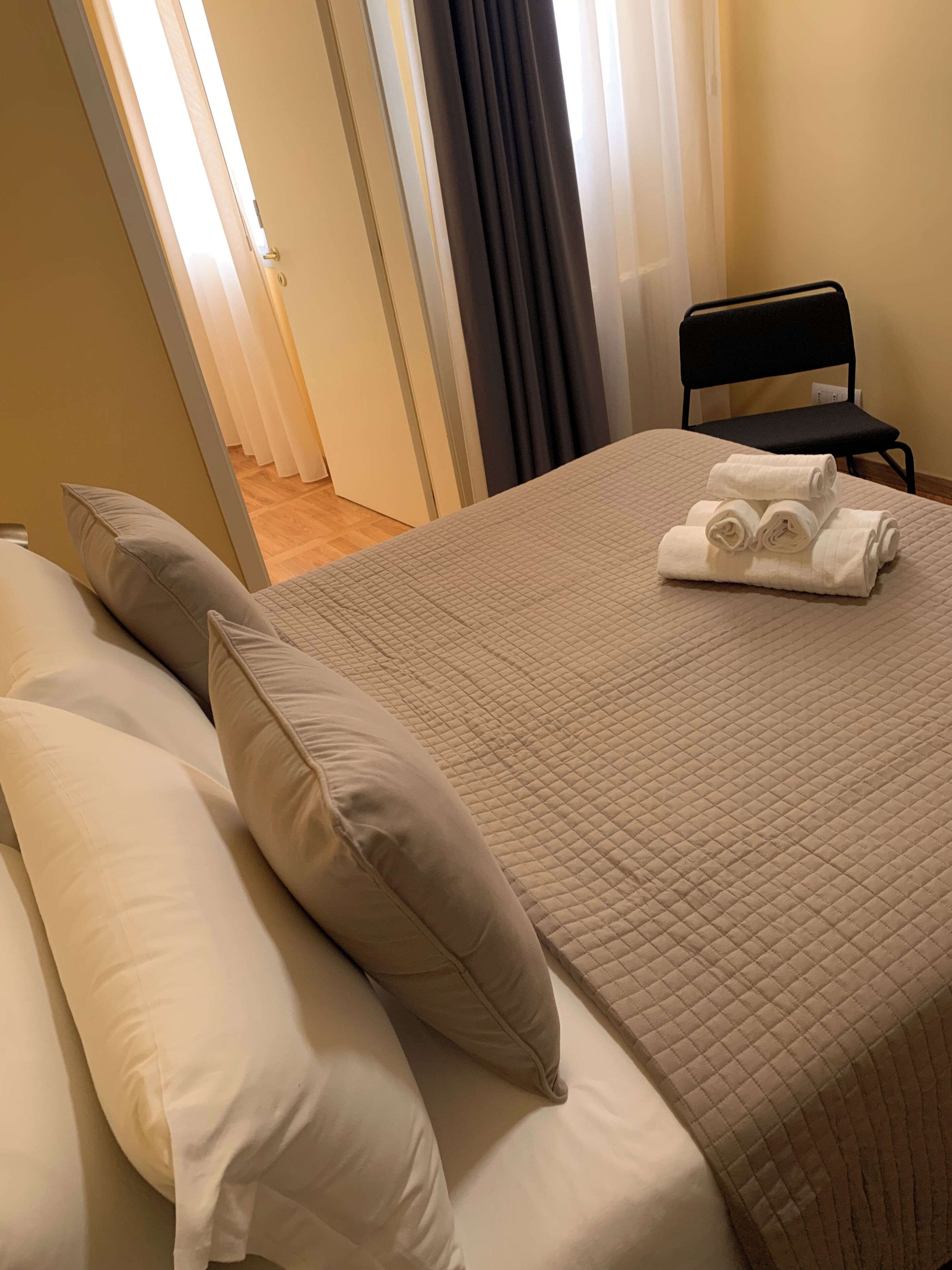 A neatly made bed with a quilted cover, two pillows, and rolled towels on the bed.