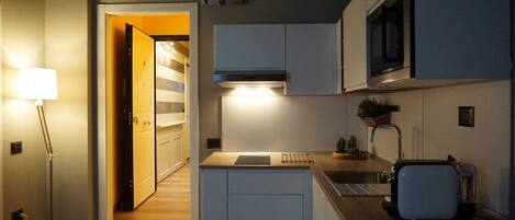Una cocina compacta con armarios blancos, un microondas, un tostador y un lavamanos.