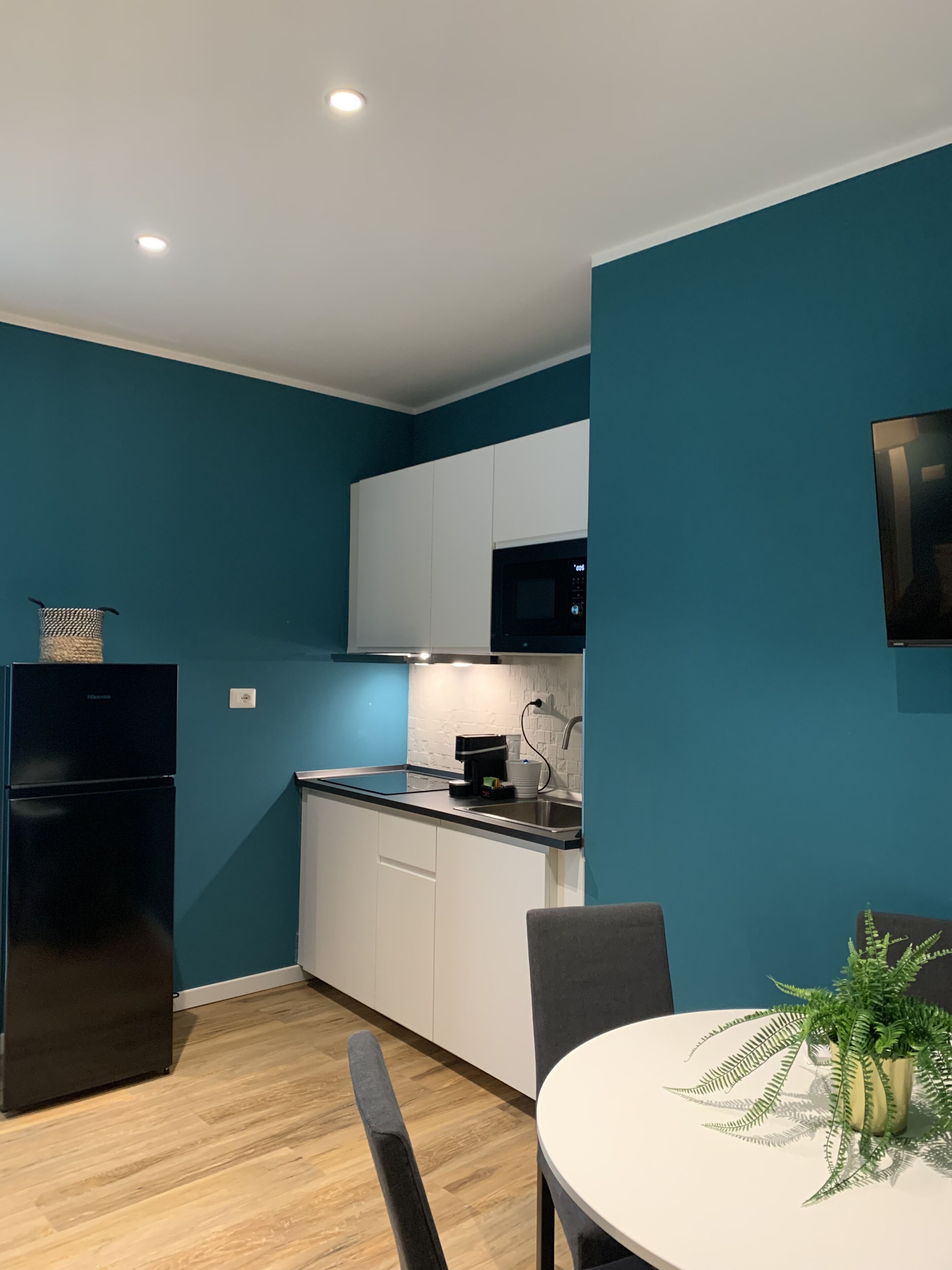 A modern kitchen with teal walls, white cabinets, a black refrigerator, and a dining area with a white table and chairs.