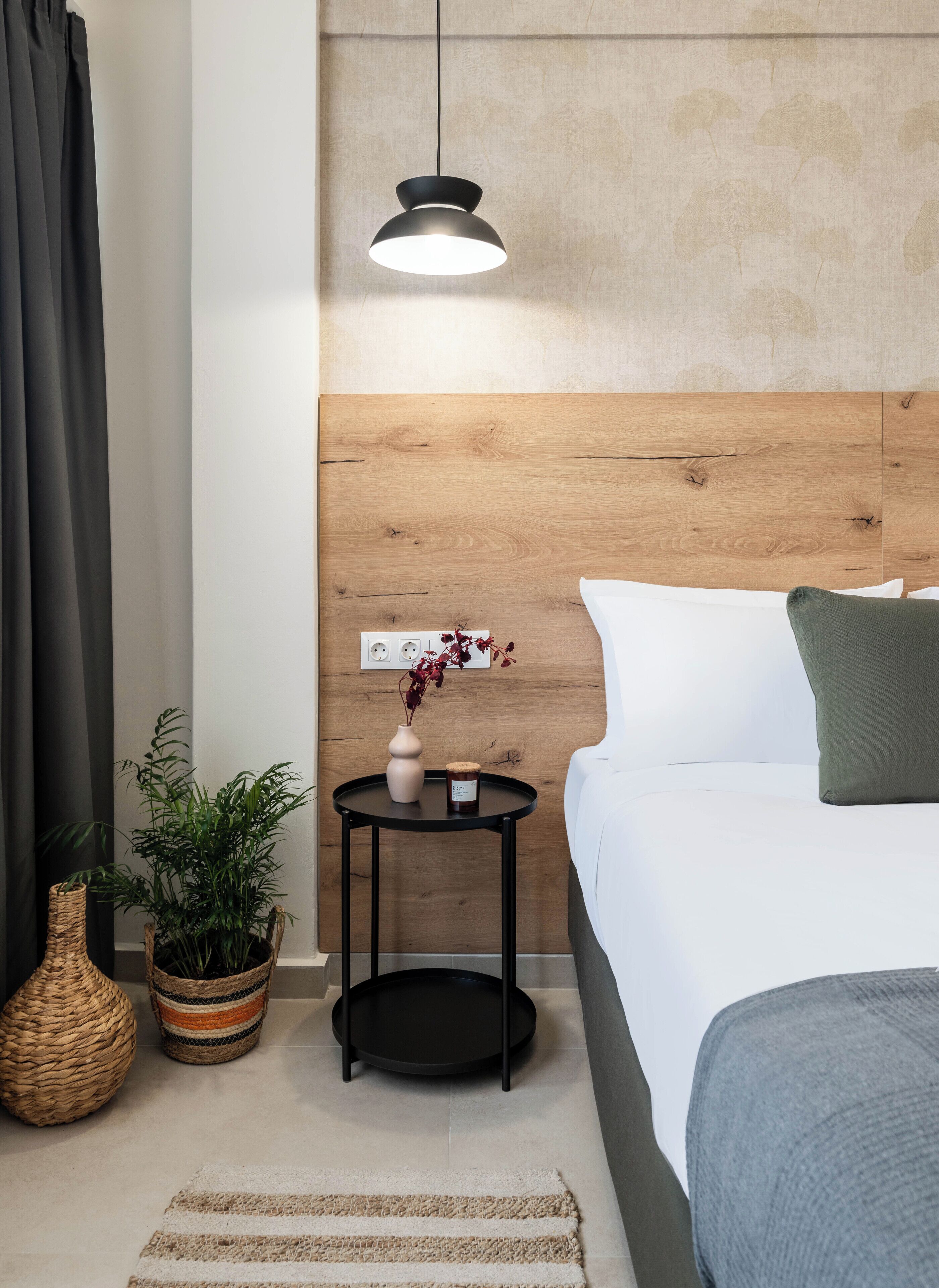 Une chambre à coucher bien aménagée, avec une tête de lit en bois, une table de chevet ornée d’un vase et d’une bougie, une suspension et un grand lit avec des oreillers.