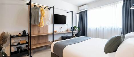 A modern hotel room with a large bed, a TV mounted on the wall, a desk with a chair, and a clothing rack.
