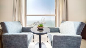 Ein Zimmer mit zwei grauen Sesseln, einem kleinen runden Tisch mit einer Pflanze und einem großen Fenster mit Blick auf eine Brücke und eine Stadtlandschaft.