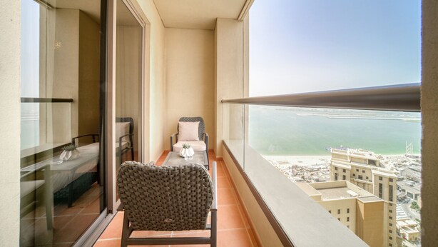 Ein Balkon mit Blick auf das Meer und Gebäude, ein Stuhl, ein kleiner Tisch und ein Bett mit Fenster.