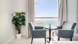 A modern room with a large window, two grey armchairs, a small round table, and a potted plant.