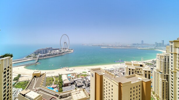 A coastal cityscape with a prominent Ferris wheel, high-rise buildings, and a beach area.