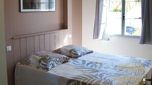 A bedroom with a bed, a window with curtains, a wall-mounted picture, and a radiator. - Superbe Maison à 150m de la Plage (Saint-Pierre-d'Oléron)