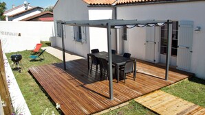 A patio with a wooden deck, a table with chairs, and a barbecue grill. - Superbe Maison à 150m de la Plage (Saint-Pierre-d'Oléron)