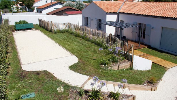 A residential property with a paved patio, a wooden deck, and a garden with raised beds and flowering plants. - Superbe Maison à 150m de la Plage (Saint-Pierre-d'Oléron)