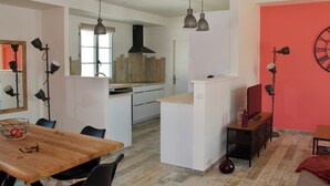 A modern kitchen with a large island, pendant lighting, and a red accent wall. - Superbe Maison à 150m de la Plage (Saint-Pierre-d'Oléron)